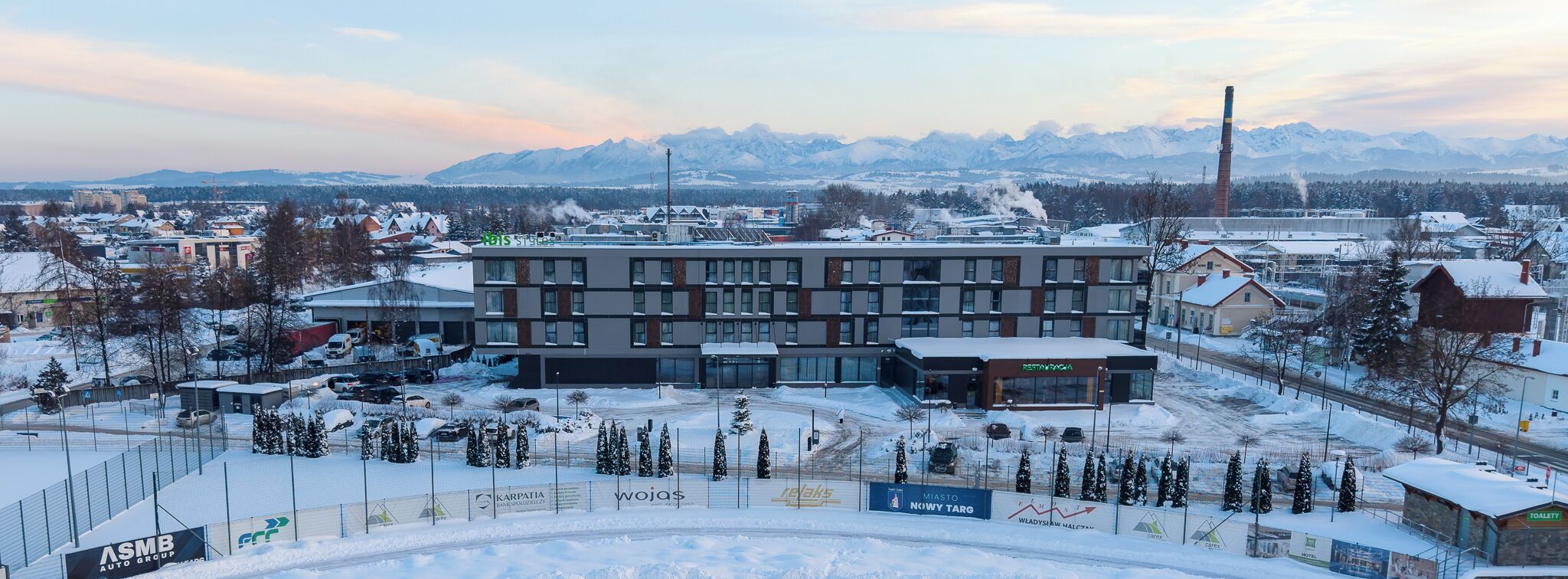 Un edificio moderno de varios pisos, rodeado de árboles cubiertos de nieve y un paisaje montañoso.