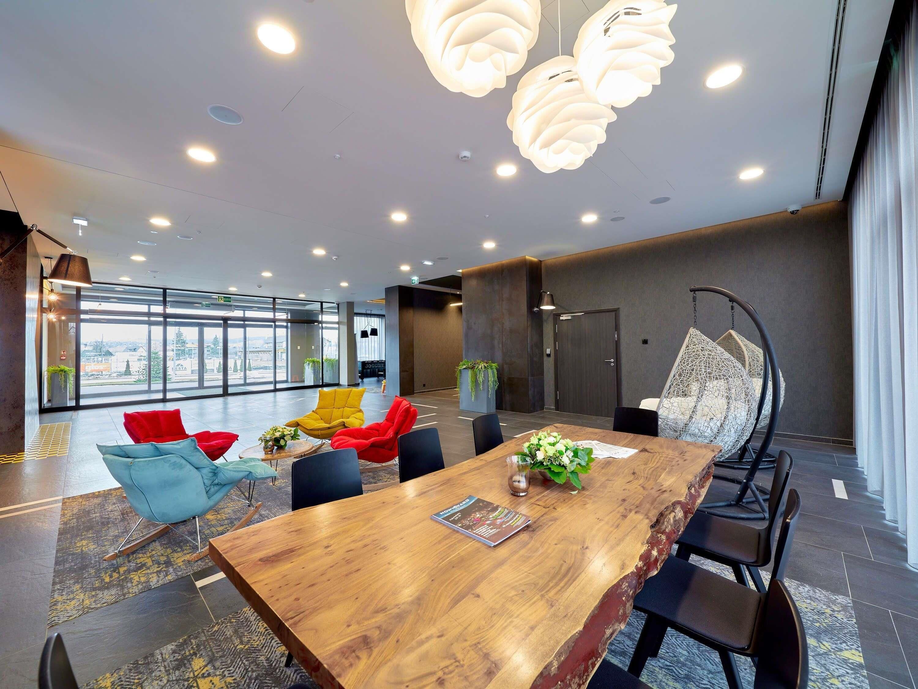 A modern conference room with a wooden table, red and blue chairs, and a hanging chair.