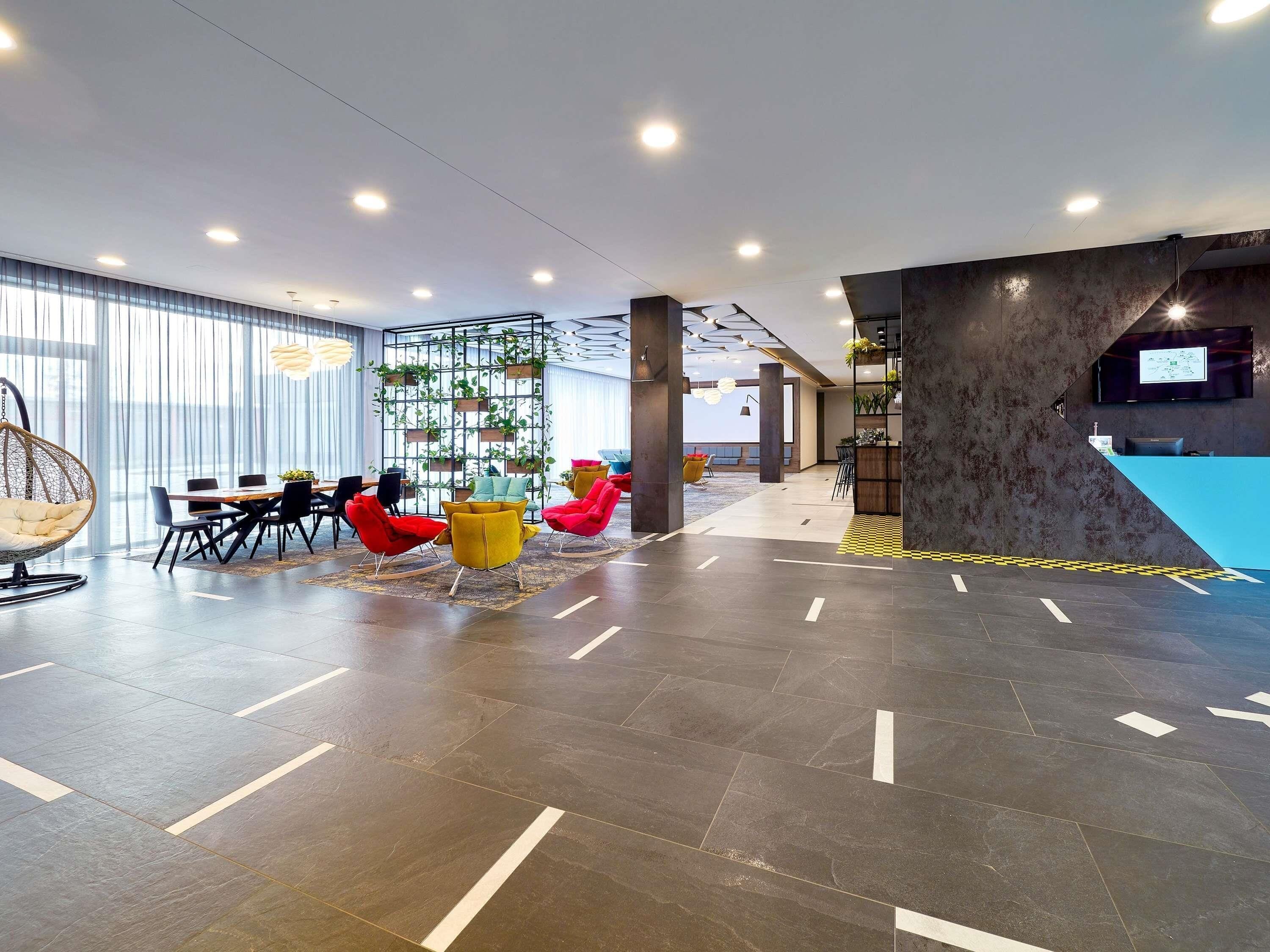 A modern interior with a dining area, colorful chairs, a reception desk, and a large window.