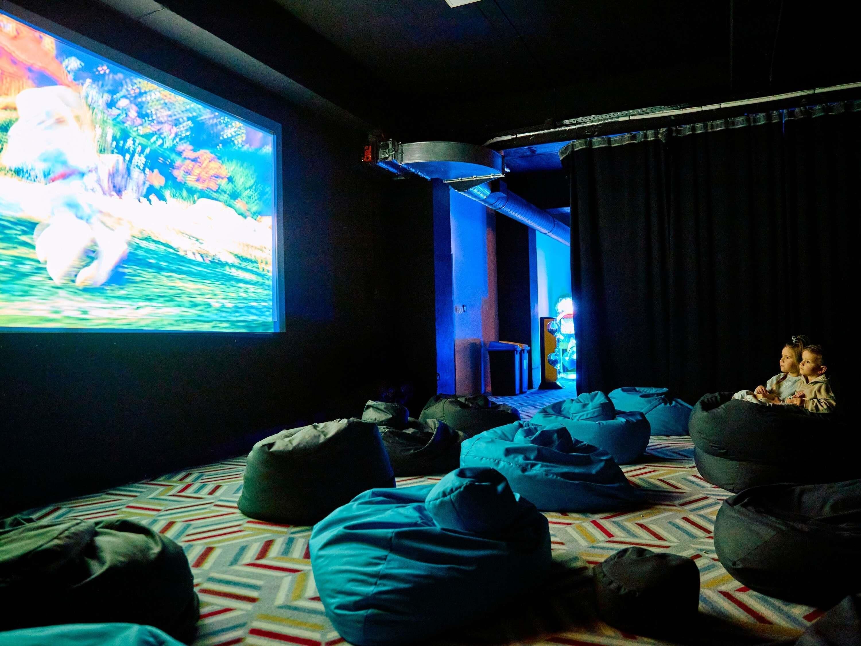 A cinema room with a large screen, bean bags, and a patterned carpet.