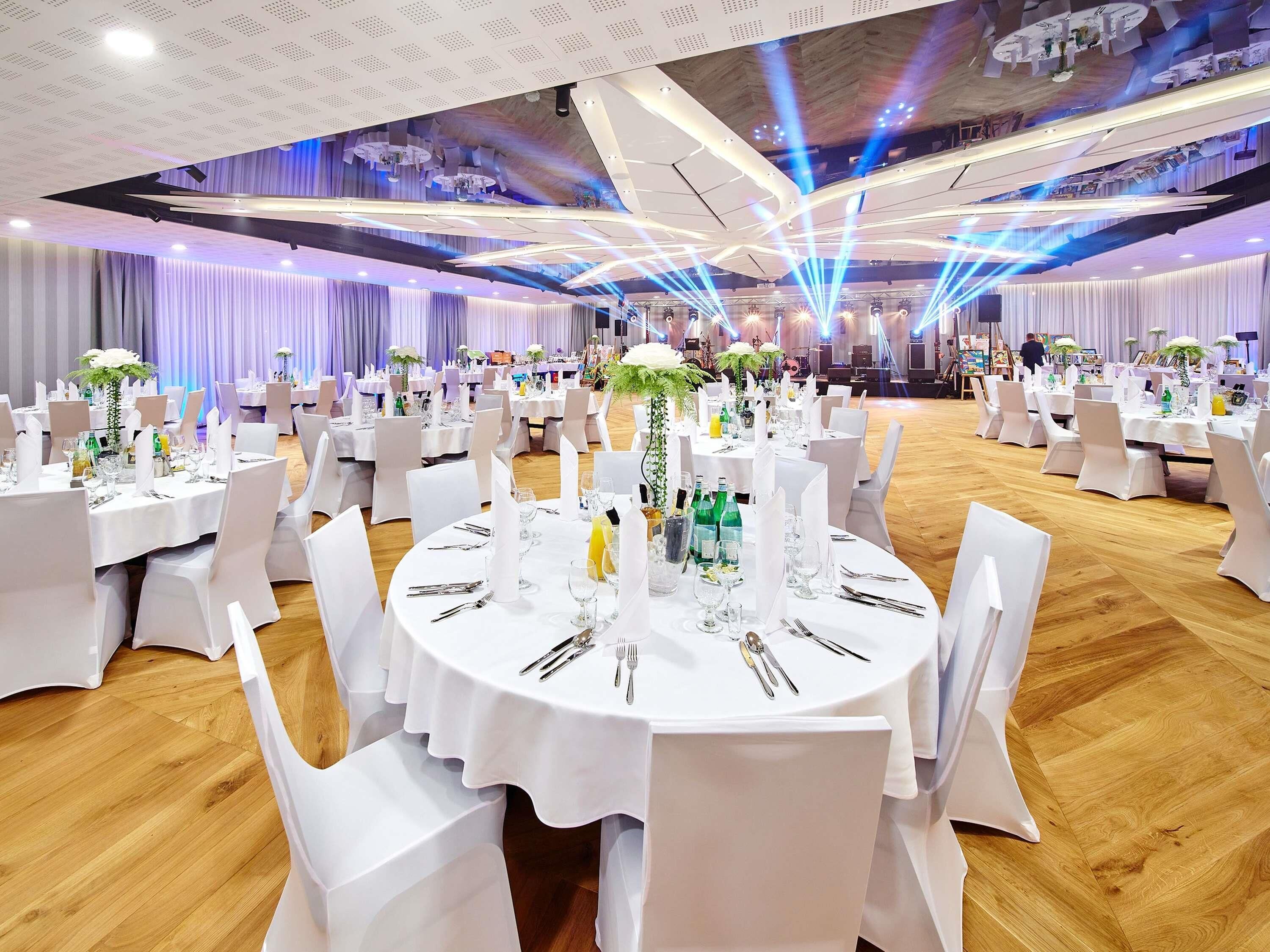A banquet hall with round tables, white tablecloths, and chairs.