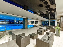 Un área de piscina interior moderna con sillones de descanso y un mostrador de recepción.