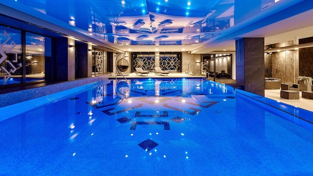 A large indoor swimming pool with a geometric tile pattern, surrounded by modern lounge areas and a high ceiling with recessed lighting. - ibis Styles Nowy Targ (Nowy Targ)