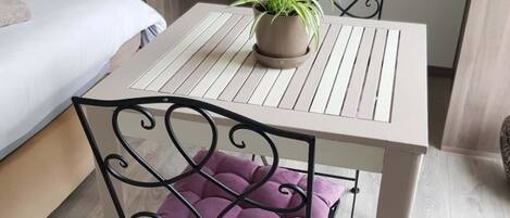 Een kleine eettafel met een bloempot, een fauteuil met kussens, en een bed op de achtergrond.