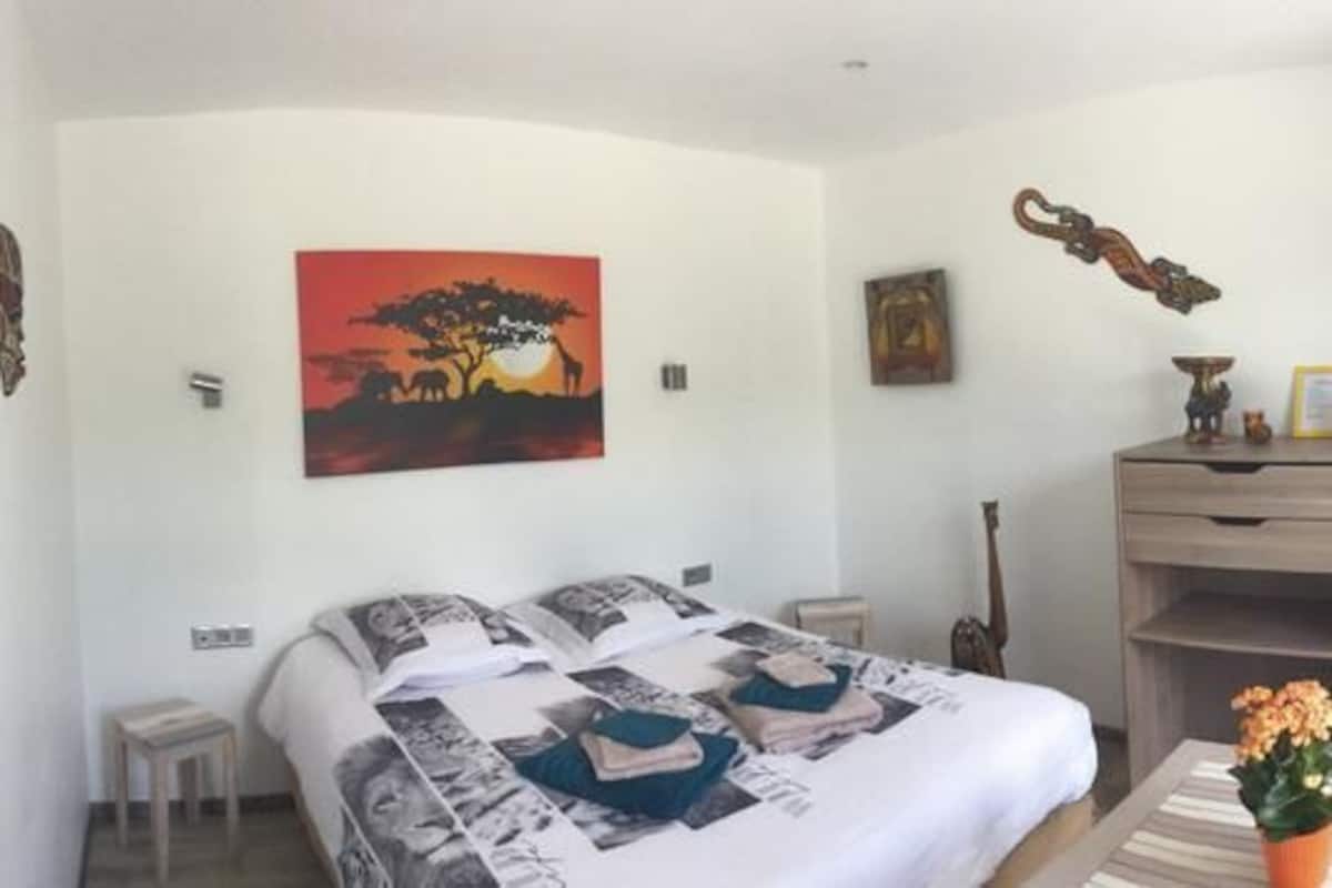 A bedroom with a bed, a desk, a chair, a small table with flowers, and a guitar.