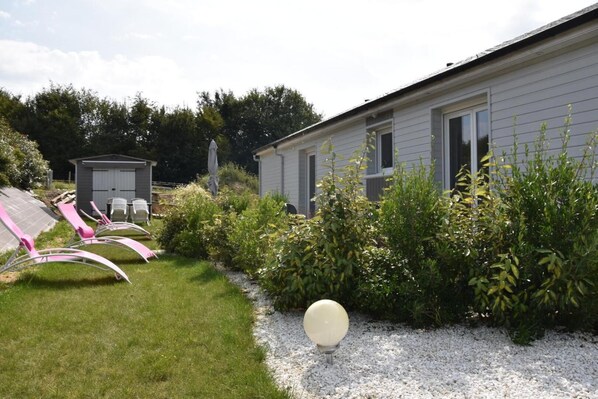 Una propiedad residencial con casa, cobertizo y jardín con sillas de jardín.