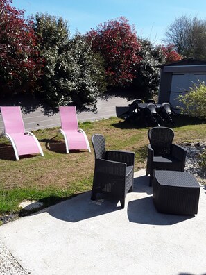 Mobiliario exterior con sillas y una mesa, un área pavimentada y un edificio al fondo.