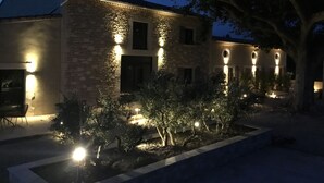 Un bâtiment en pierre doté de nombreuses fenêtres illuminées et d’un jardin bien éclairé.