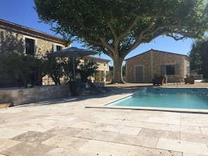 A stone building with a pool, outdoor seating, and a large tree providing shade. - Le Mas de Nonin - Chambres d'hotes (Noves)