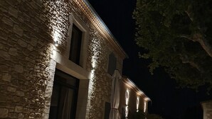 Un bâtiment en pierre doté d’un éclairage extérieur soigné, d’un espace de repos couvert et d’un arbre en arrière-plan.