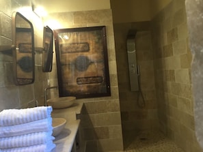 A bathroom with a stone wall, a sink with a bowl, a mirror, and a shower. - Le Mas de Nonin - Chambres d'hotes (Noves)