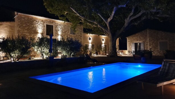 Un bâtiment en pierre avec une piscine, illuminé par un éclairage d’ambiance, de nuit.