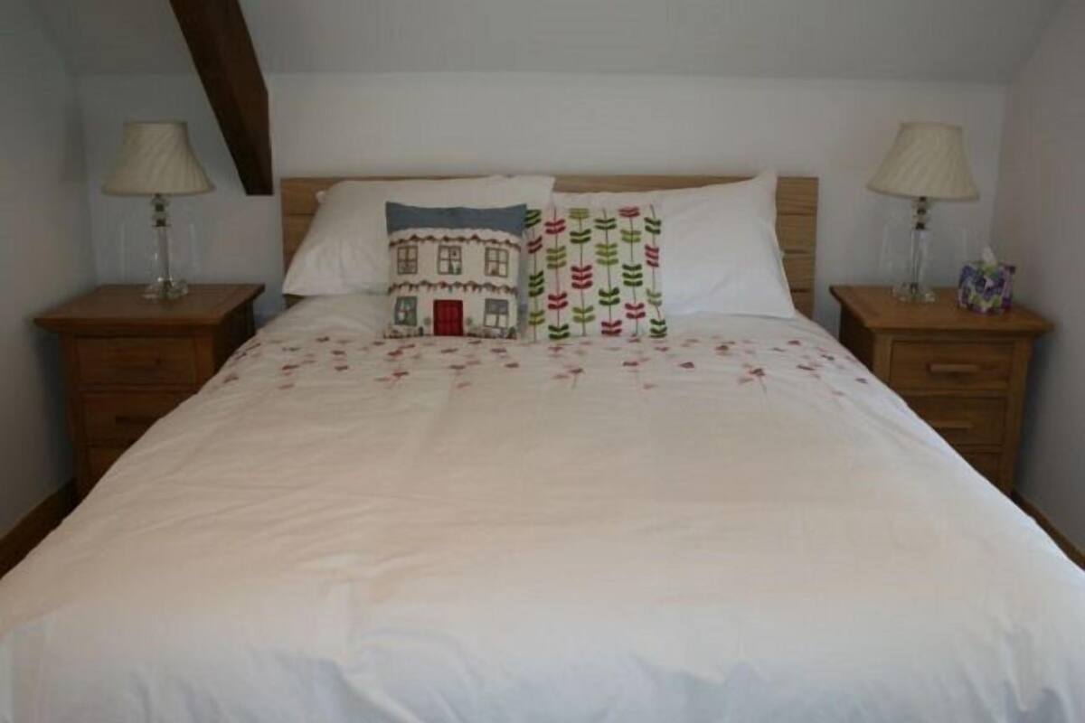 A neatly made bed with white bedding and two decorative pillows, flanked by wooden nightstands with lamps.