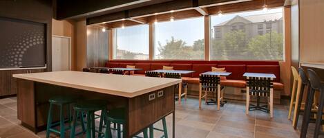 A modern dining area with a long table, multiple booths, and a large window providing a view of buildings and trees.