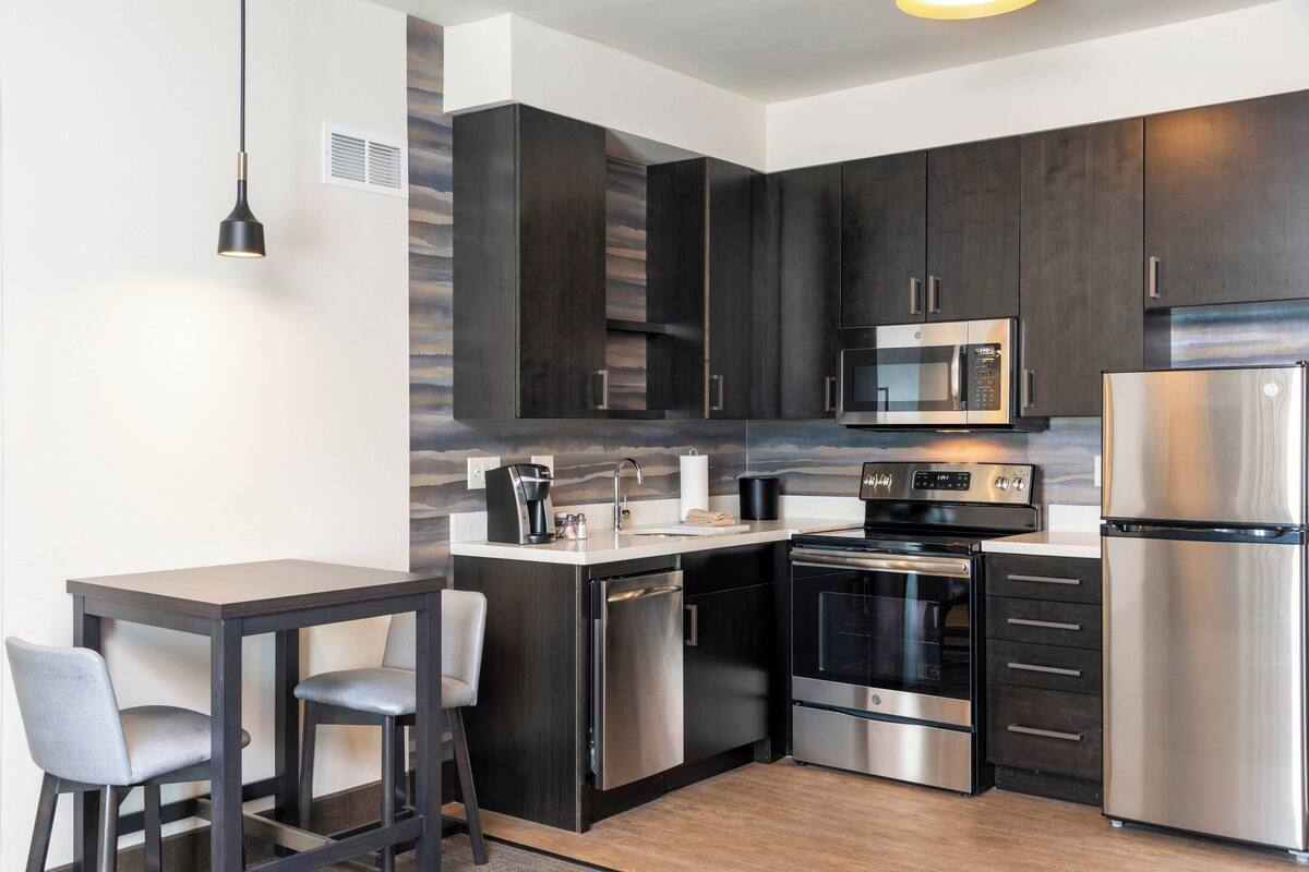 A modern kitchen with dark cabinetry, stainless steel appliances, and a small dining area with two chairs.