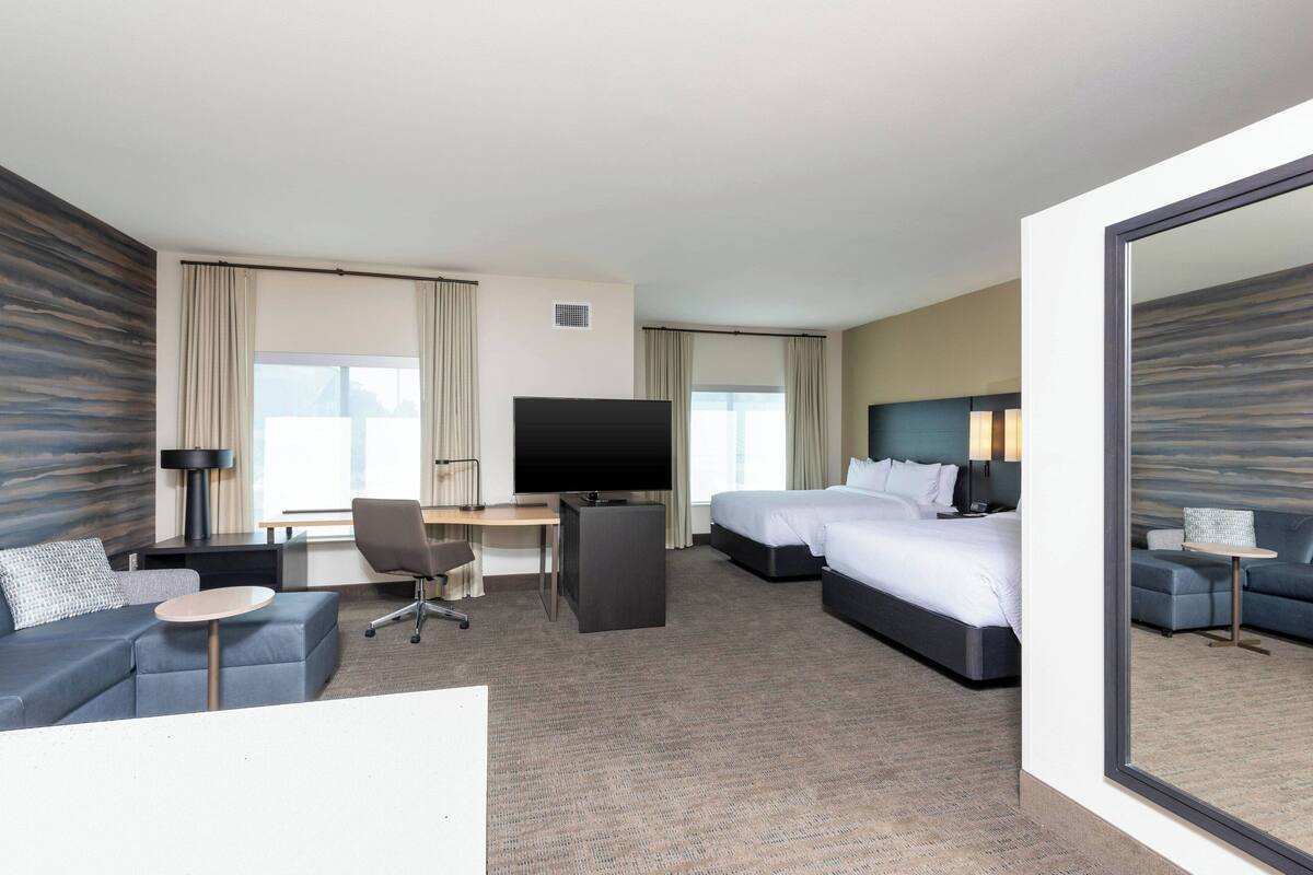 A hotel room with a large bed, a desk with a TV, a sofa, and a small table.