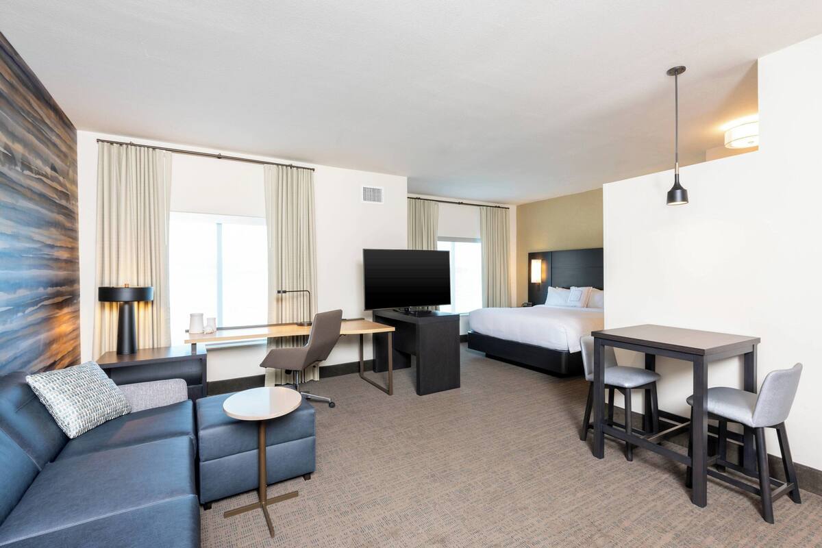 A hotel room with a sofa, a desk, a bed, and a TV.
