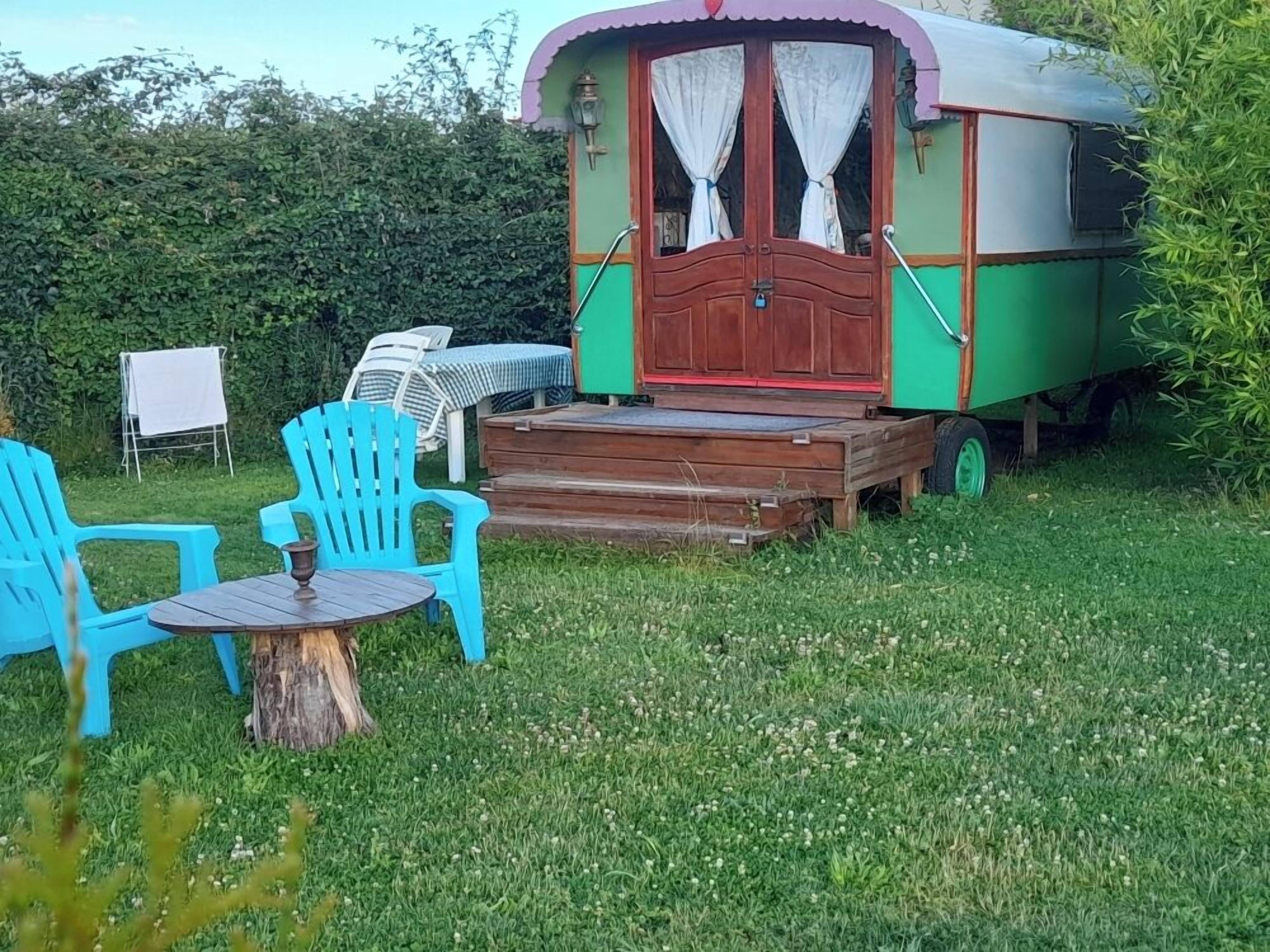 A green and red mobile home with a porch, two blue chairs, and a small table.