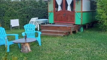 A green and red mobile home with a porch, two blue chairs, and a small table.