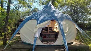 A tent with a wooden deck entrance, a bed inside, and a view of the surrounding forest. - Le Clos des Epinettes (Angé)