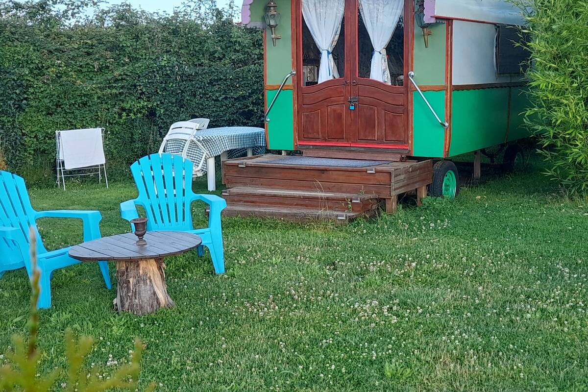 A green and red trailer with a wooden deck, two blue chairs, and a small table.