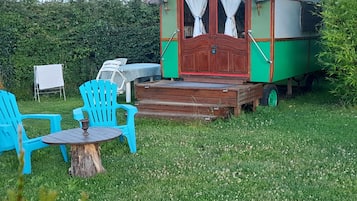 A green and red trailer with a wooden deck, two blue chairs, and a small table.