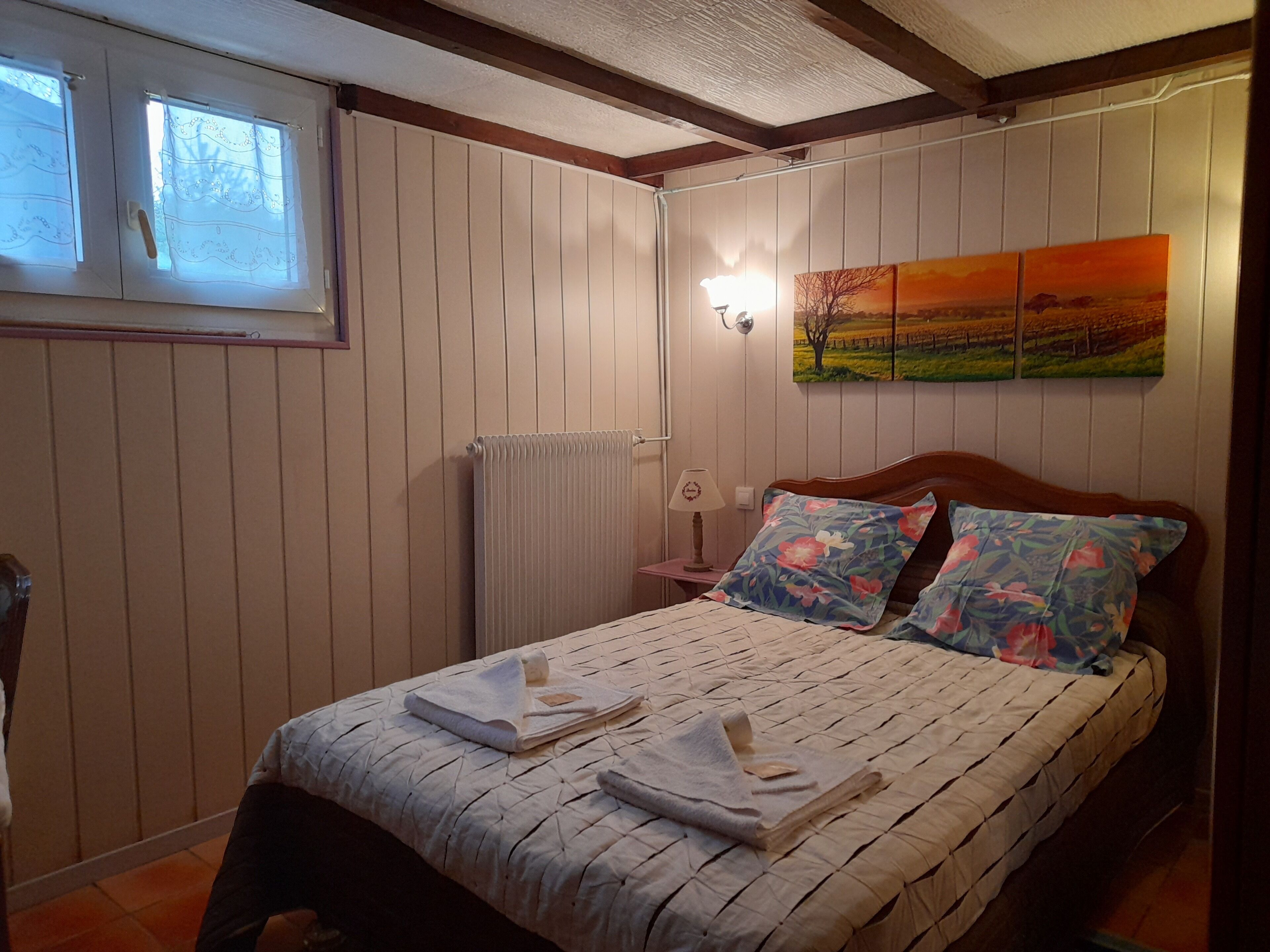 Un dormitorio con cama, un radiador, una mesita de noche, una lámpara y una ventana con cortinas.