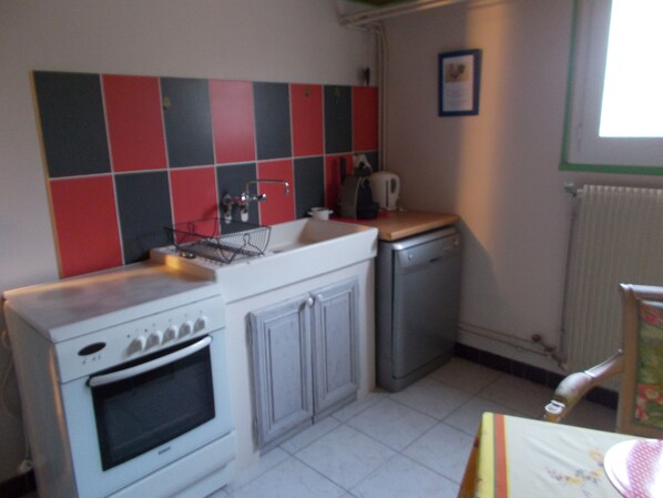 Una cocina compacta con estufa blanca, un lavamanos pequeño y un lavavajillas. Se observa un salpicadero de azulejos rojos y negros sobre el lavamanos.