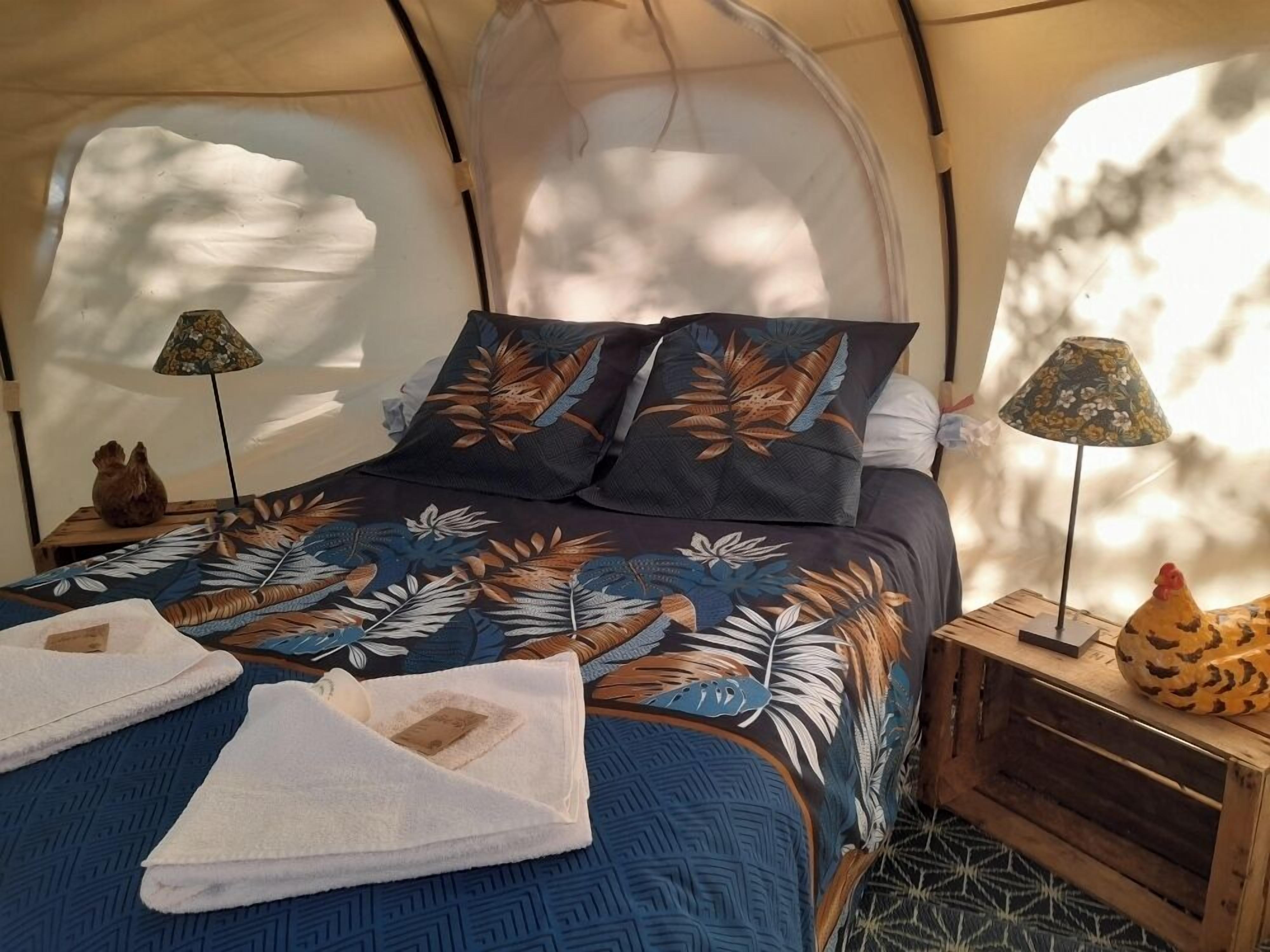 A tented room with a bed, two lamps, and a decorative chicken on a side table.