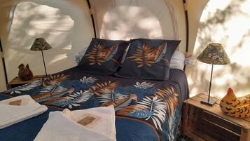 A tented room with a bed, two lamps, and a decorative chicken on a side table.