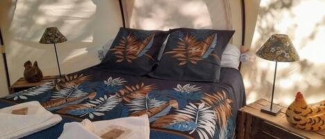 Una habitación con tienda de campaña, una cama, dos lámparas y un pollo decorativo sobre una mesita.