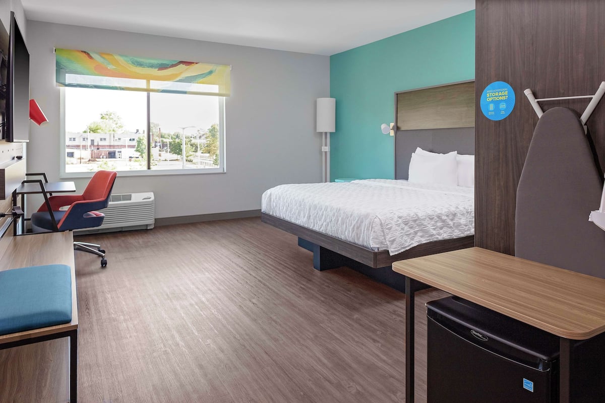 A hotel room with a bed, a desk, a chair, a heater, a window with a view, and a storage sign.