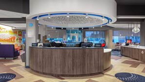 Una moderna zona de recepción de hotel con un mostrador circular, varias estaciones de trabajo con computadoras y vistas de la ciudad a través de amplias ventanas.