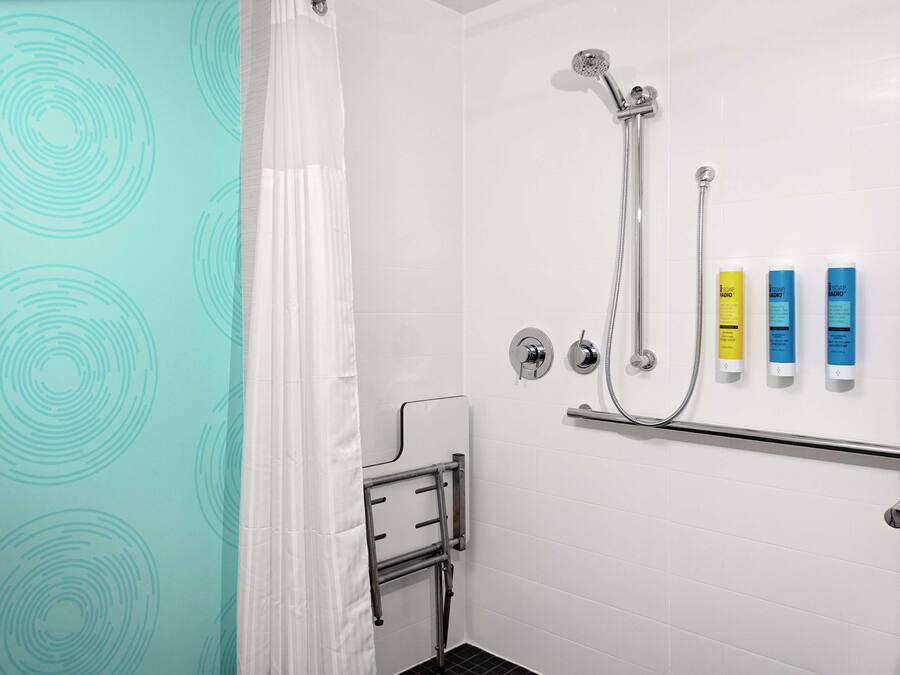 A bathroom with a shower, a grab bar, and three toiletries on the wall.