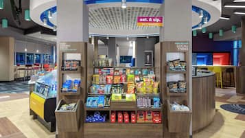 Pieni myyntikioski, jossa on tarjolla erilaisia pakattuja elintarvikkeita ja juomia, kyltti, joka ilmoittaa, että lähikauppa on auki ympäri vuorokauden, sekä myyntitiski paikallisille tuotteille.