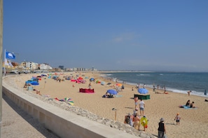 Una playa con gente, sombrillas y edificios al fondo.