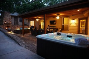 A hot tub in a covered outdoor area with stone steps leading up to a stone fireplace. - Tuscan Retreat | Hot Tub | Amazing Location (Fredericksburg)