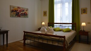 Een keurig opgemaakt slaapkamer met een bed, nachtkastje, lamp, een schilderij aan de muur en een raam met gordijnen.