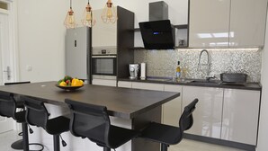 Een moderne keuken met een centraal eiland, barstoelen, een ingebouwde oven en hangende lampen.