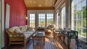 Una habitación soleada con pared roja, techo de madera y ventanas amplias que ofrecen vistas a la vegetación y montañas.