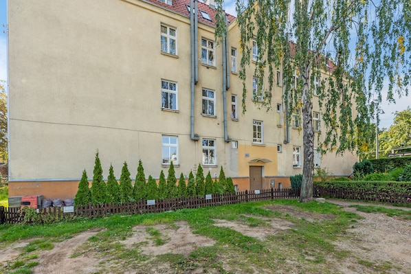A multi-story building with a beige facade, multiple windows, and a small garden area with neatly trimmed bushes and a wooden fence. - Grand Apartments - Love Loft (Sopot)