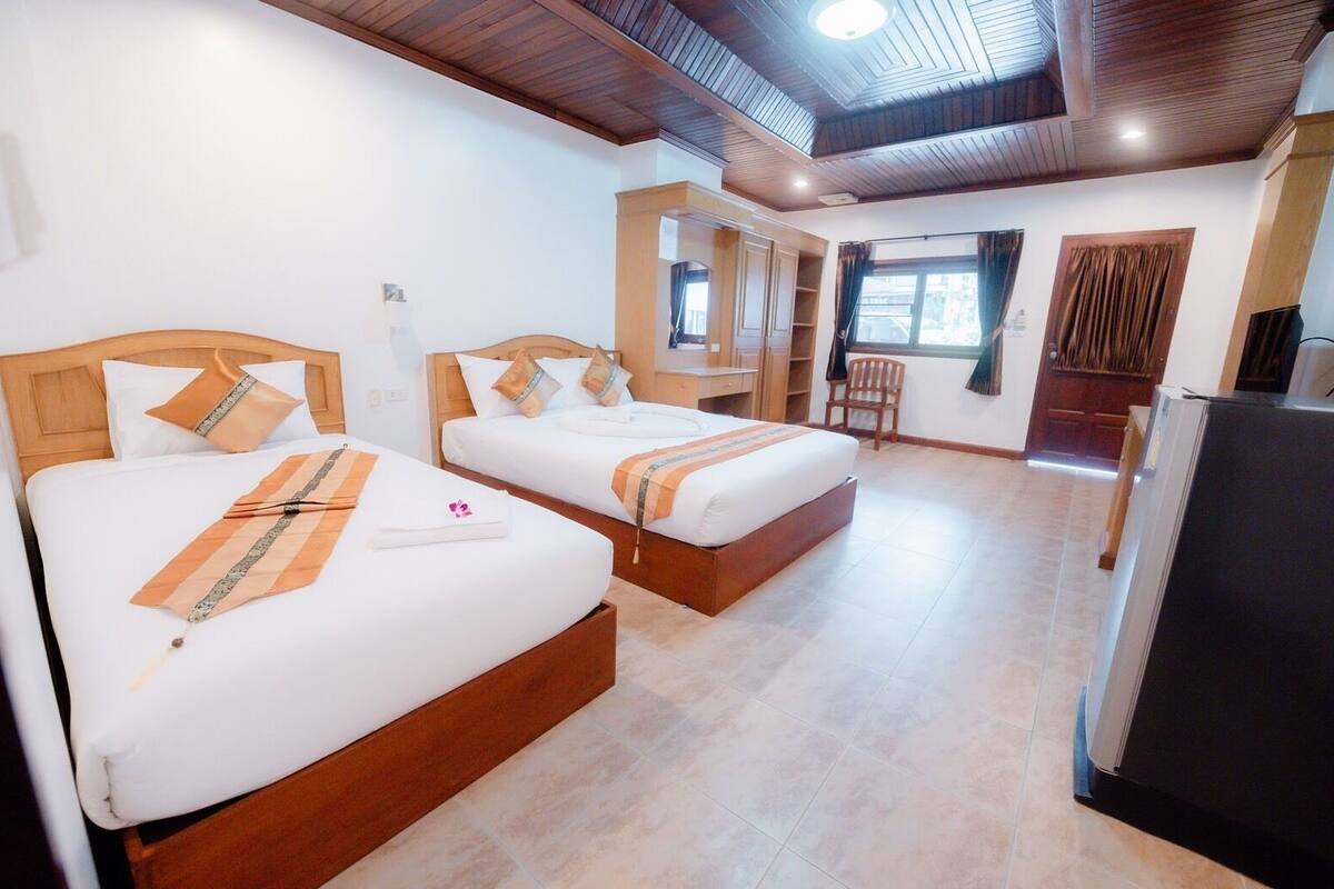 A hotel room with two beds, a desk, a chair, and a refrigerator.