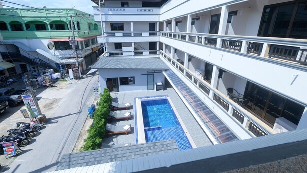 A multi-story hotel with a rooftop pool, balconies, and a view of the street below. - Coconut  Grove Hotel Samui - Hostel (Koh Samui)