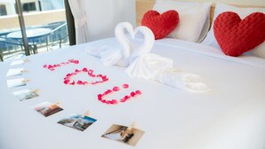 A neatly made bed with heart-shaped decorations and photos, a balcony with a table, and a city view. - Coconut  Grove Hotel Samui - Hostel (Koh Samui)