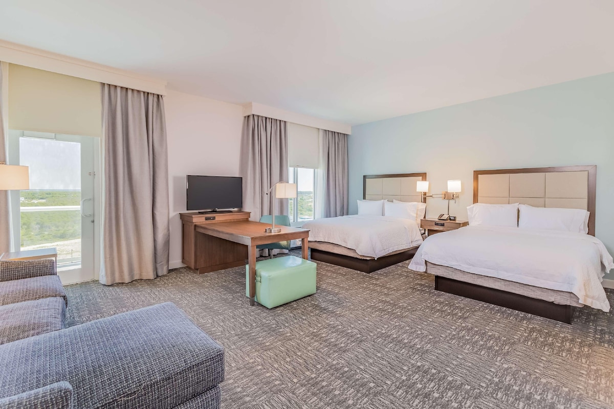 Habitación de hotel con cama, dos mesitas de noche, un escritorio, una silla, una maleta y un televisor.