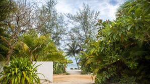 A pathway leading to a beach with palm trees and a white wall on the left. - Mittali Hotel (Sihanoukville)