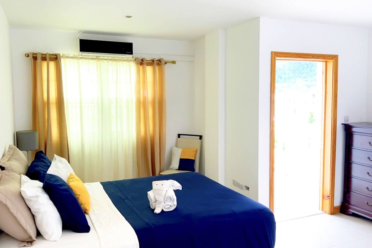 Une chambre d’hôtel avec un lit, une table de chevet, une lampe, une commode et une fenêtre avec des rideaux.
