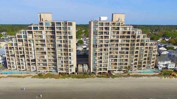 Un edificio residencial alto con varios balcones, techo plano y vista a la playa.