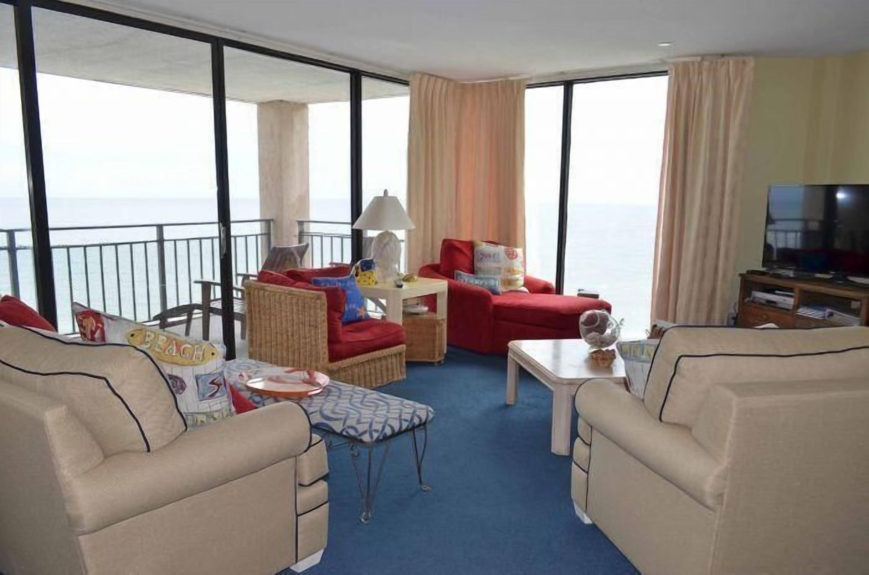 Un balcón amplio con vistas al mar, amoblado con sofás color beige, una mesita y un televisor.