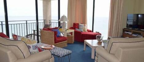 Un balcón amplio con vistas al mar, amoblado con sofás color beige, una mesita y un televisor.